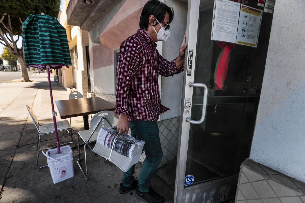A man opens a door holding a large stack of newspapers