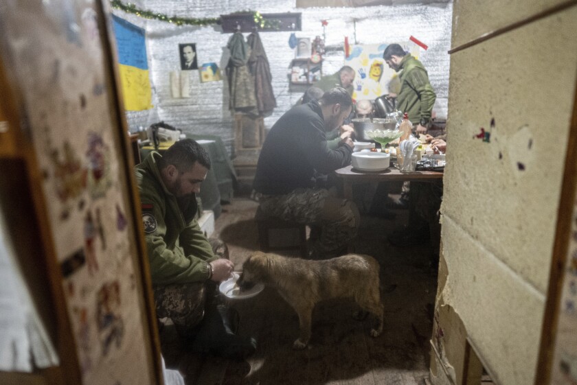 A Ukrainian serviceman feeds his dog as other soldiers eat in a shelter at the frontline positions near Zolote, Ukraine