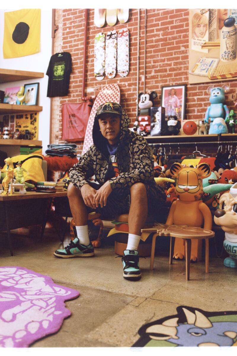 A seated man in a hoodie and shorts in a store with a brick wall.