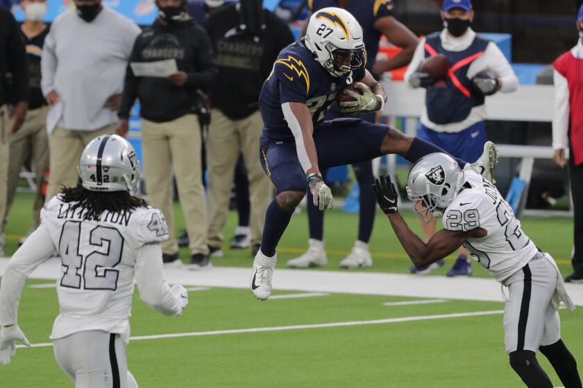 INGLEWOOD, CA - NOVEMBER 8, 2020: Los Angeles Chargers running back Joshua Kelley (27) tries to leap over the oncoming Las Vegas Raiders free safety Lamarcus Joyner (29) in the 4th quarter at SoFi Stadium on November 8, 2020 in Inglewood, CA.(Gina Ferazzi / Los Angeles Times)