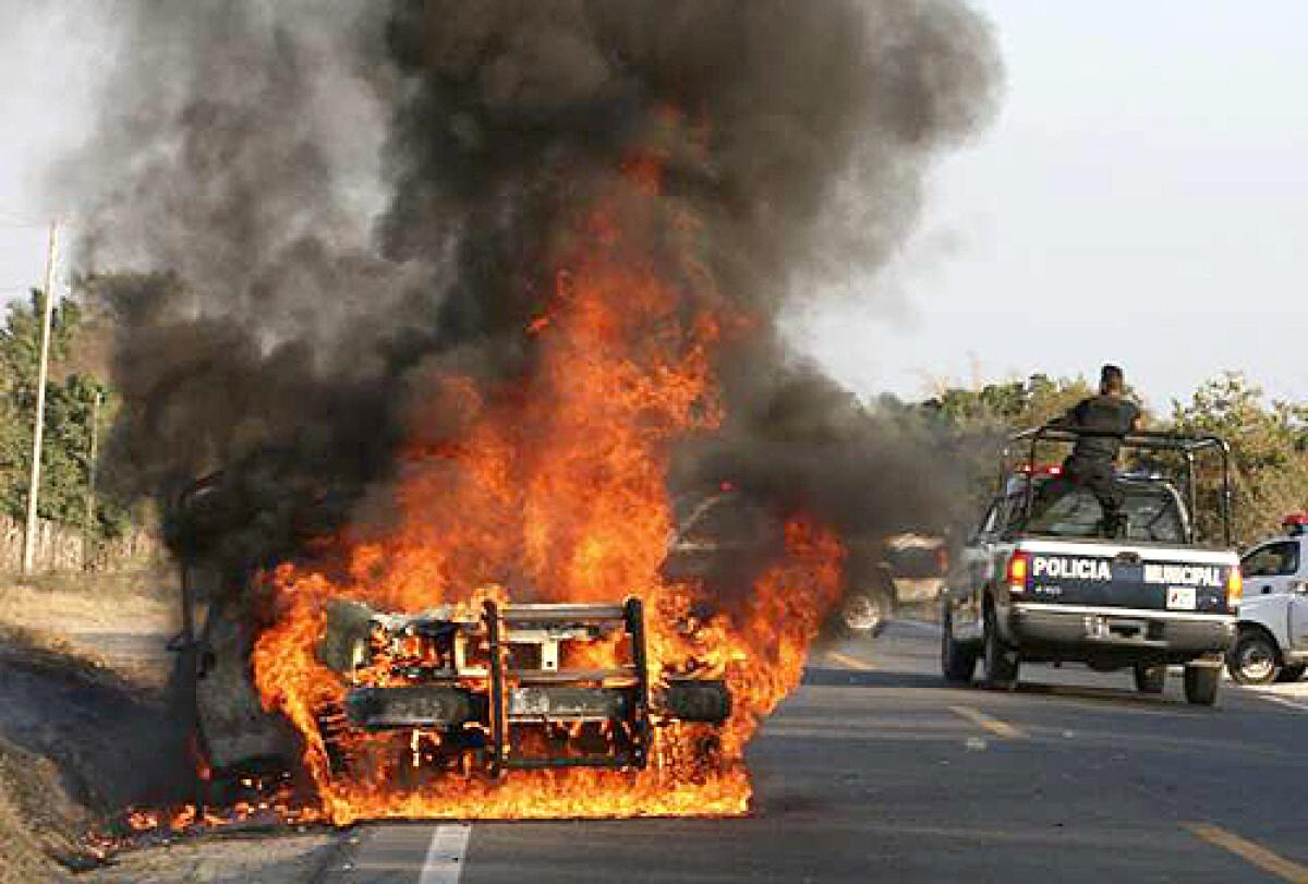 Police officers drive past a burning police vehicle in Zihuatanejo, Mexico. In a three-week period, five grenade attacks were launched on police patrols and stations.