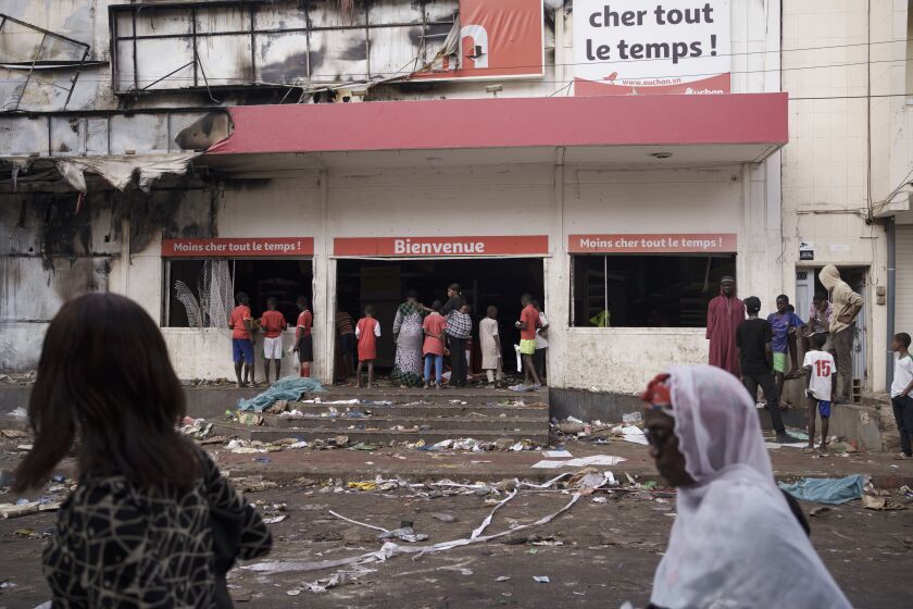 People stand at the entrance of a destroyed supermarket in Dakar, Senegal, Saturday, June 3, 2023. Senegal's government says at least nine people have been killed in violent clashes between police and supporters of opposition leader Ousmane Sonko, with authorities issuing a blanket ban on the use of several social media platforms in the aftermath of the violence. (AP Photo/Leo Correa)