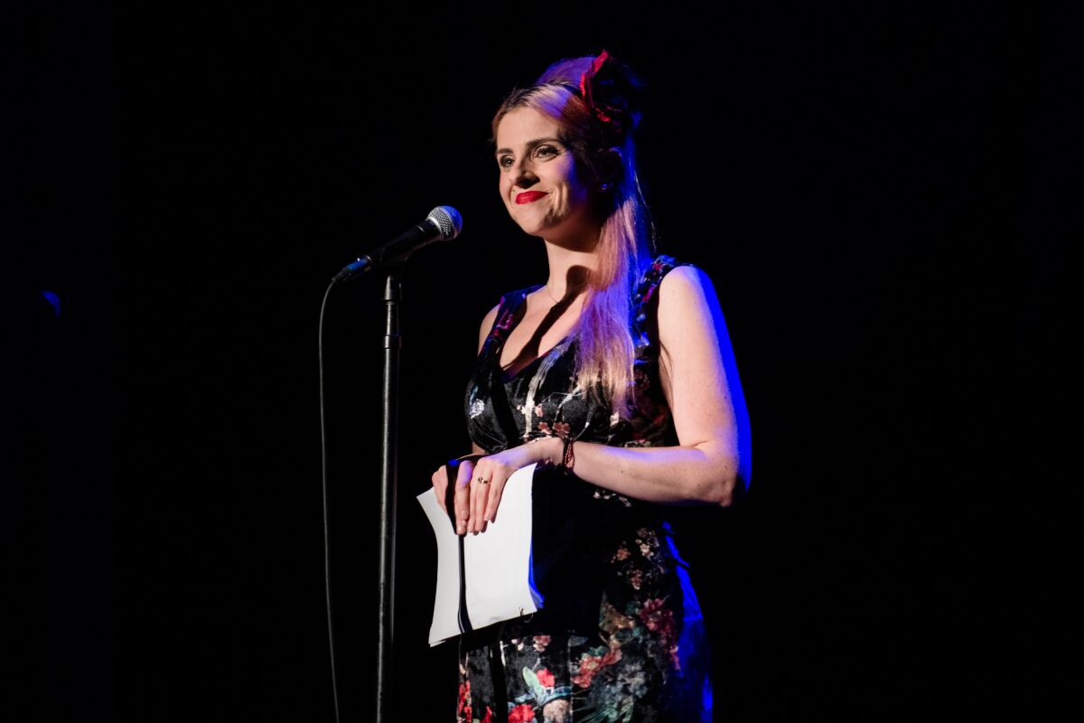 A woman at a microphone holds a script.