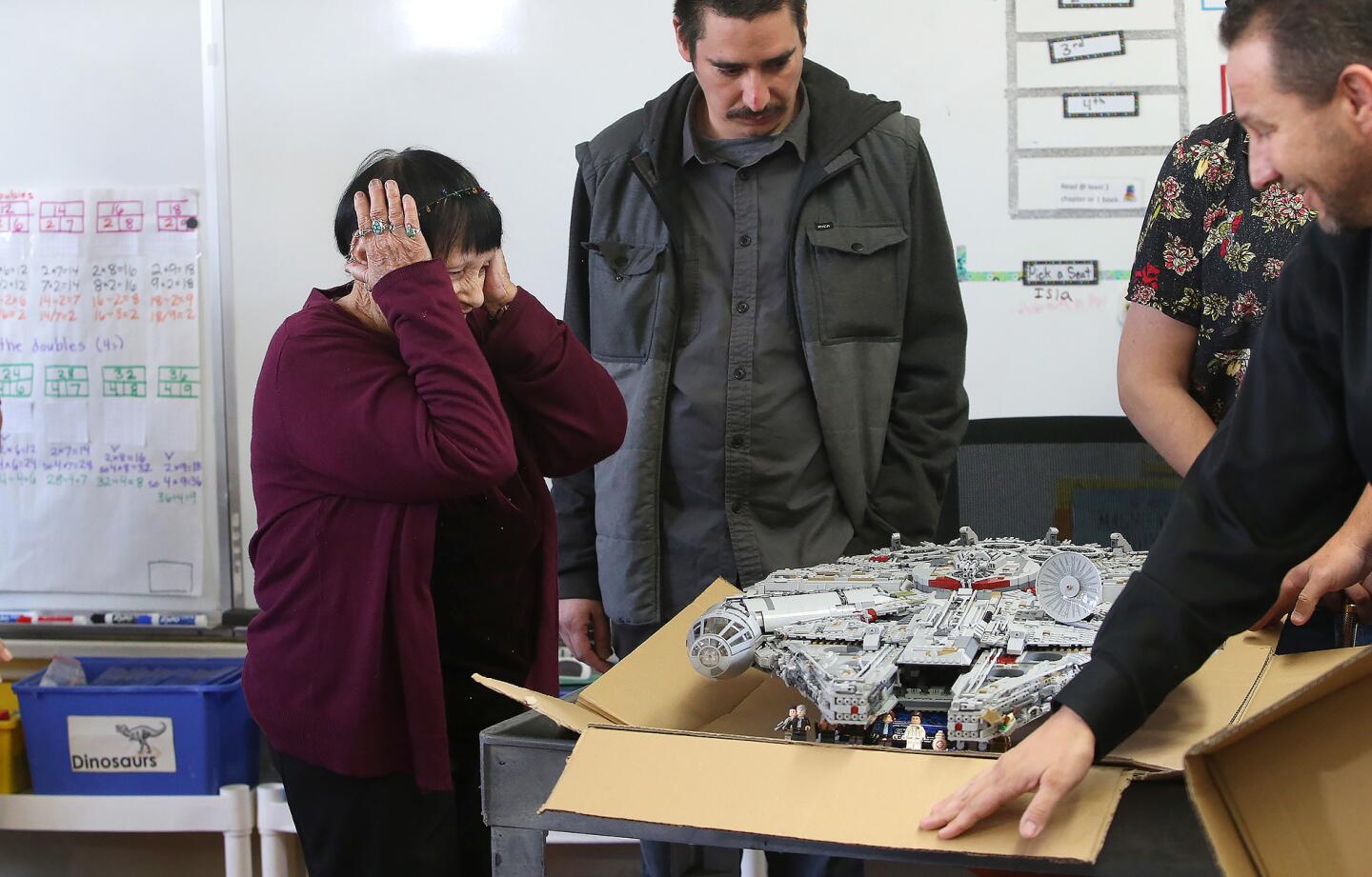 Instructional assistant Jeanna Bassett reacts upon seeing her lego millennium falcon starship unveiled by folks from Goodwill, including Ted Mollenkramer, far right, after it was damaged by vandals at Concordia Elementary in San Clemente. Master Lego builder Scott Gano from Goodwill who helped rebuild the Star Wars ship, stands next to her.