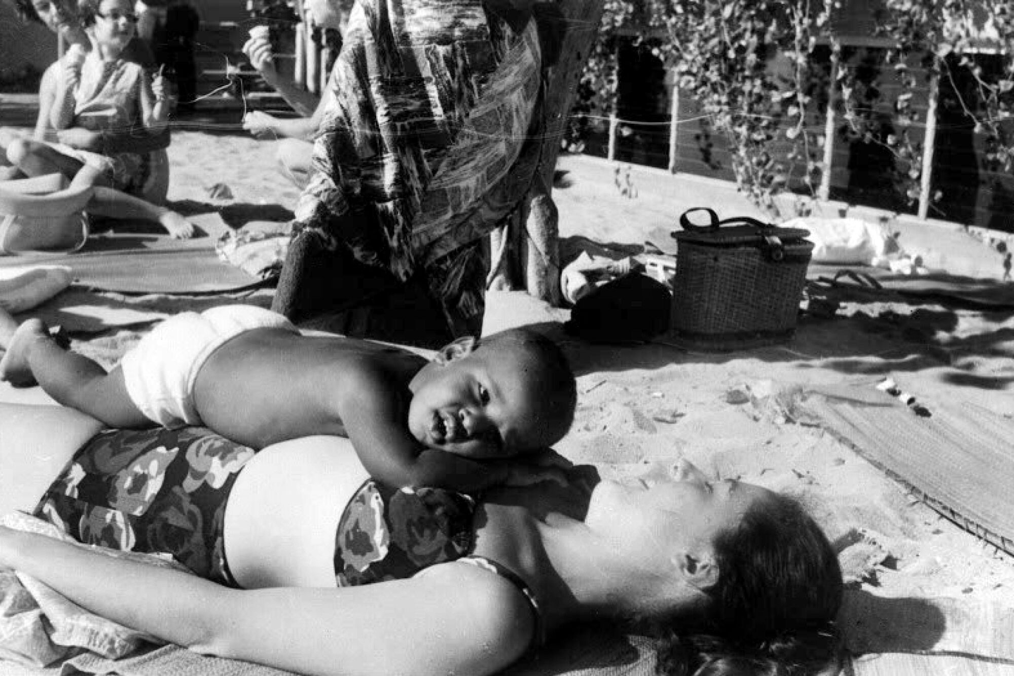 A small child lies on its mother's torso as she lies on the beach in Hawaii