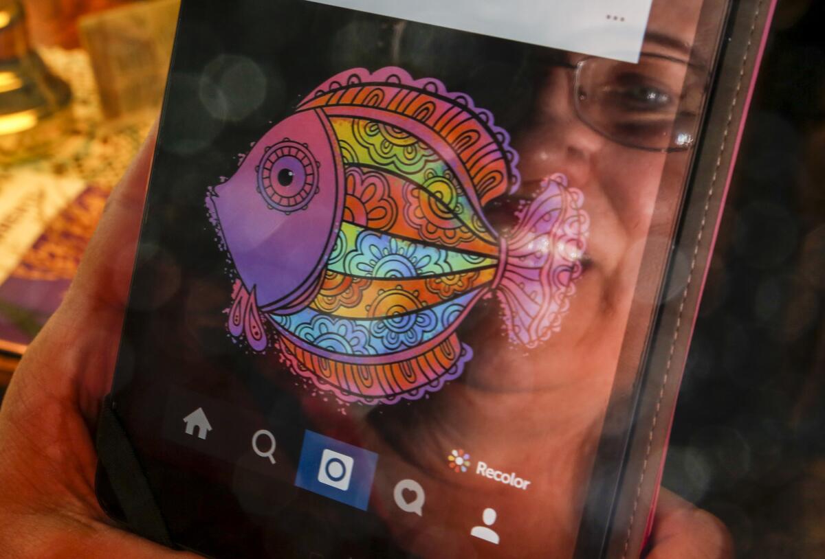 At home in Long Beach, Cheri Brown is reflected on the screen of her iPad Mini where she makes vibrant graphic designs using the coloring app Recolor.