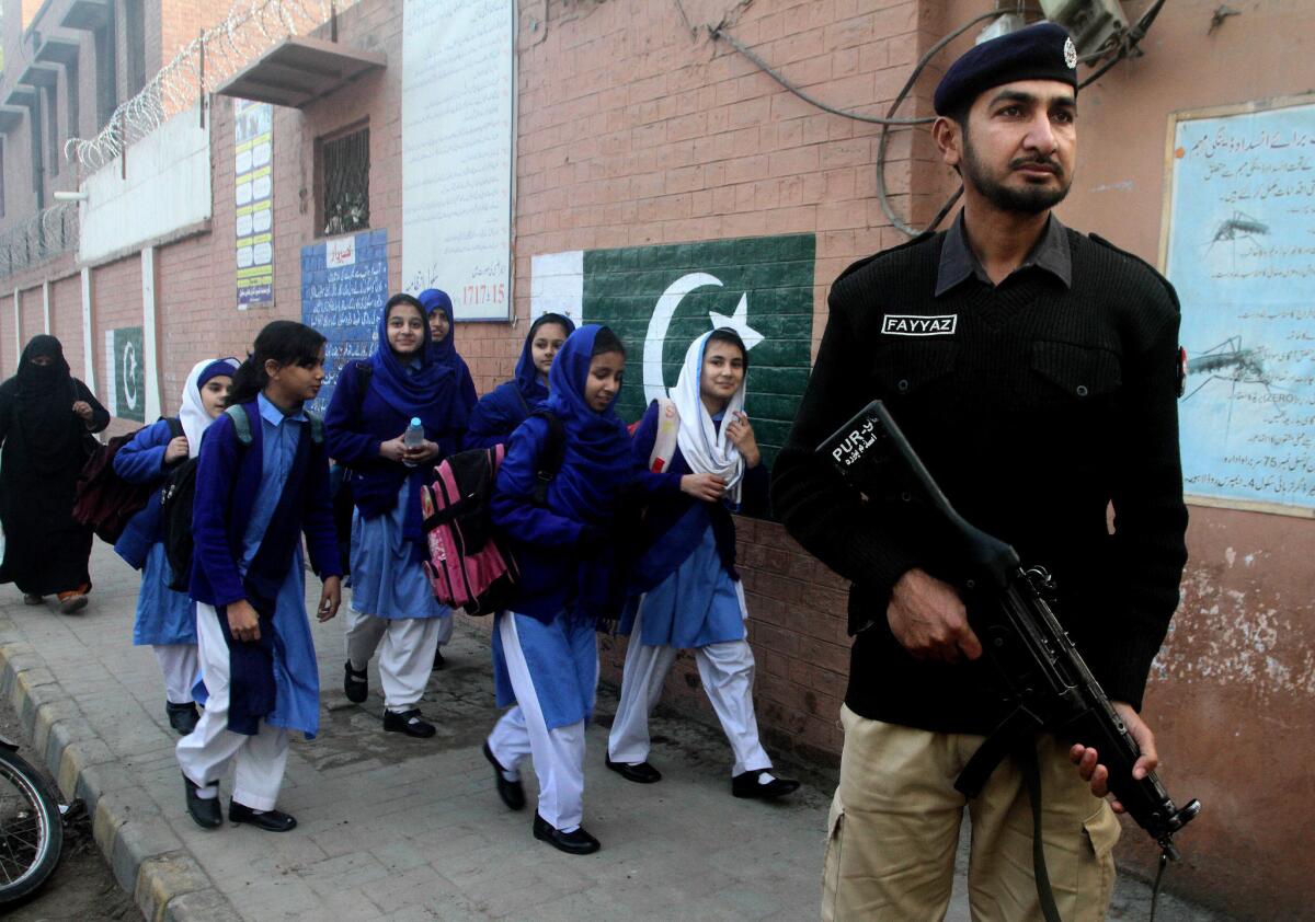 A Pakistani police officer stands guard as children make their way to school in Lahore, Pakistan, on Monday.