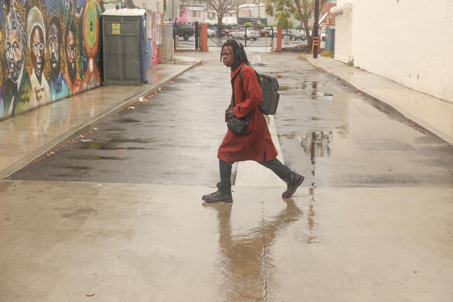 Los Angeles, CA - March 22: A person walks on the street with a coat during a rainy morning at Leimerk Park Plaza on Friday, March 22, 2024 in Los Angeles, CA. (Michael Blackshire / Los Angeles Times)