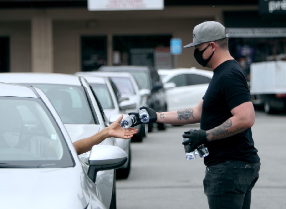 With a long line of cars waiting at Strut Bar & Club, general manager Aaron Reid passes out bottles of water before handing out lunch bags during Wednesday's free meals event.