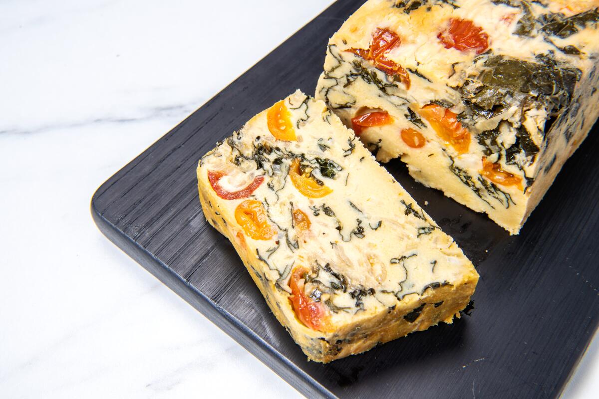 A slice sits next to a loaf-shaped Chickpea Frittata With Tomatoes and Kale