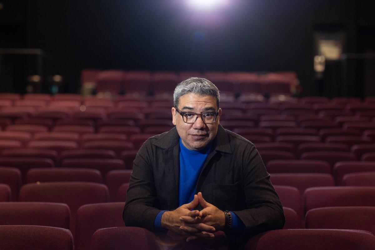 A man in a blue shirt and a blazer sits in a movie theater.
