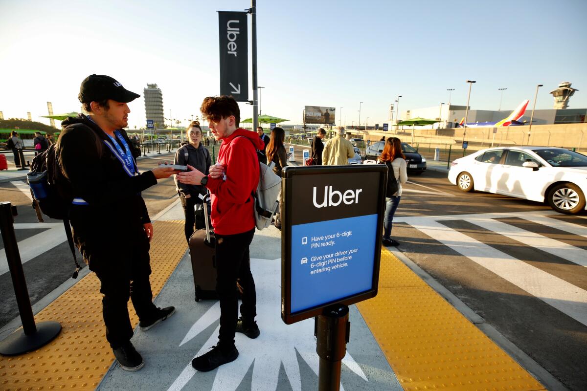 Alex Geddo left, with Uber, helps passenger Kaleb Brewer, arriving from Oklahoma, at the new LAX passenger pickup lot on Oct. 29, the first day of the new ride-hailing change.