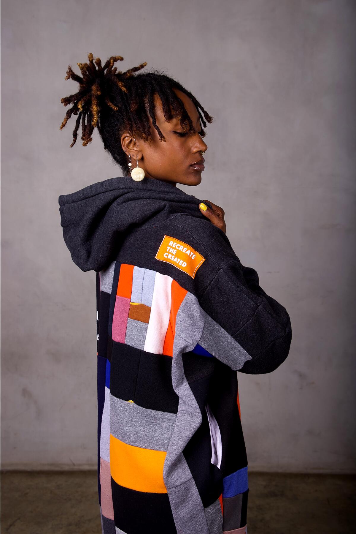 A woman wearing an upcycled, multicolored hoodie. 