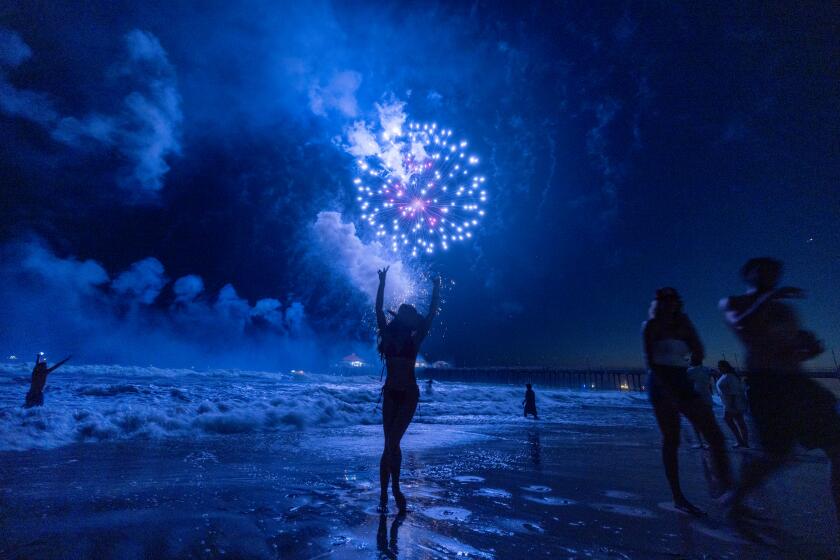Huntington Beach, CA - July 04: Carli Dugan, of San Louis Obispo, dances in the water while watching the sky light up with fireworks over the ocean and pier on Independence Day, 4th of July in Huntington Beach Thursday, July 4, 2024. (Allen J. Schaben / Los Angeles Times)