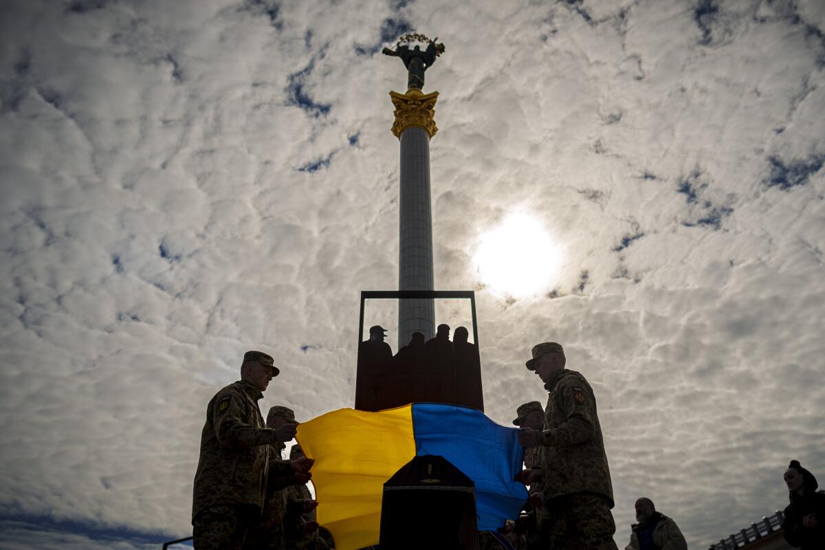 Ukrainian servicemembers place the national flag on a coffin in Independence Square in Kyiv.