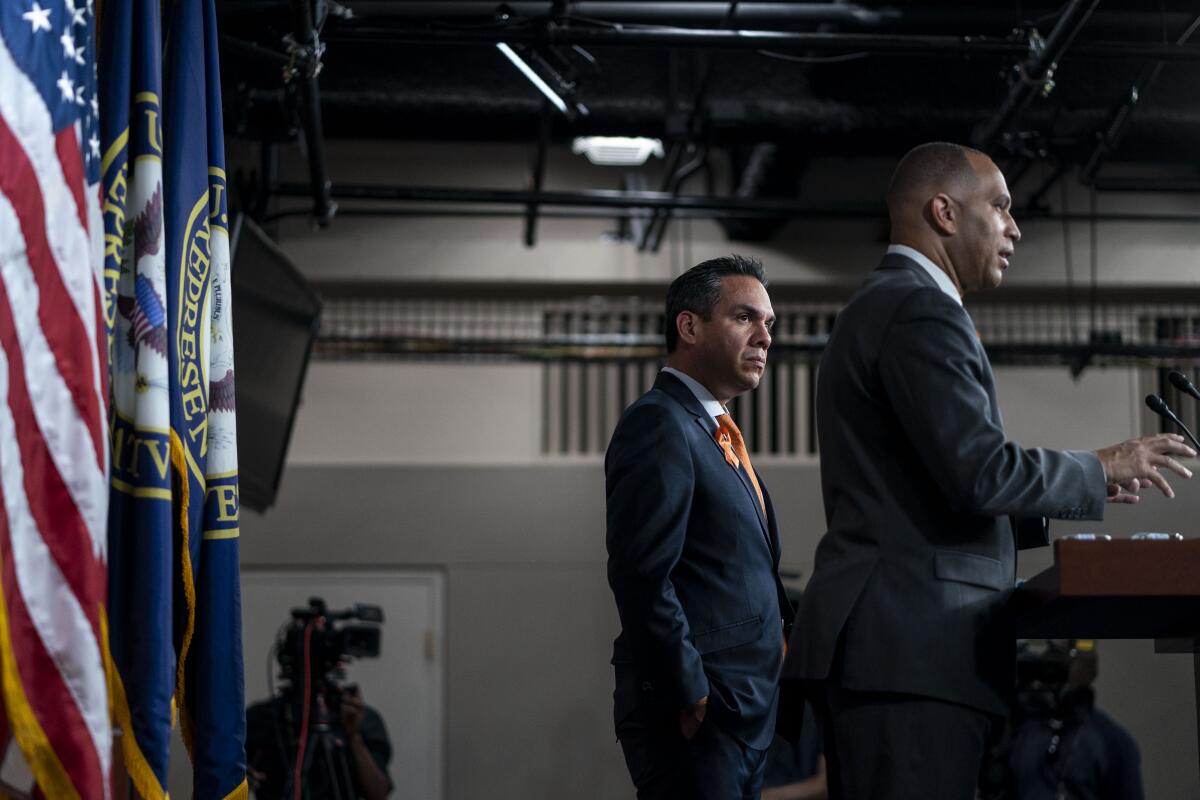 A man standing by as another man speaks during a news conference.