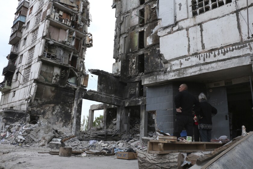 Residentes, parados junto a edificios gravemente dañados por los intentos combates en Mariúpol,