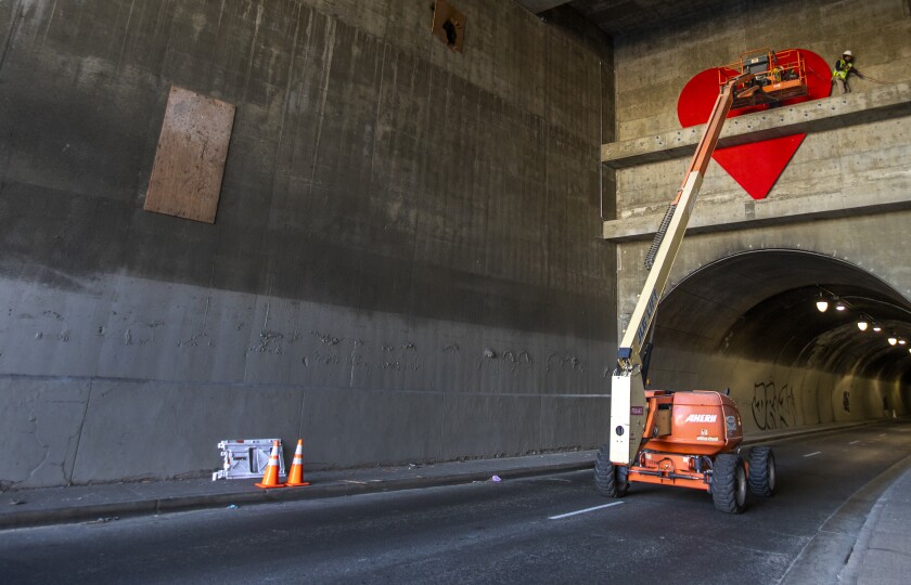 Des ouvriers installent un grand cœur rouge au-dessus d'une extrémité d'un tunnel.