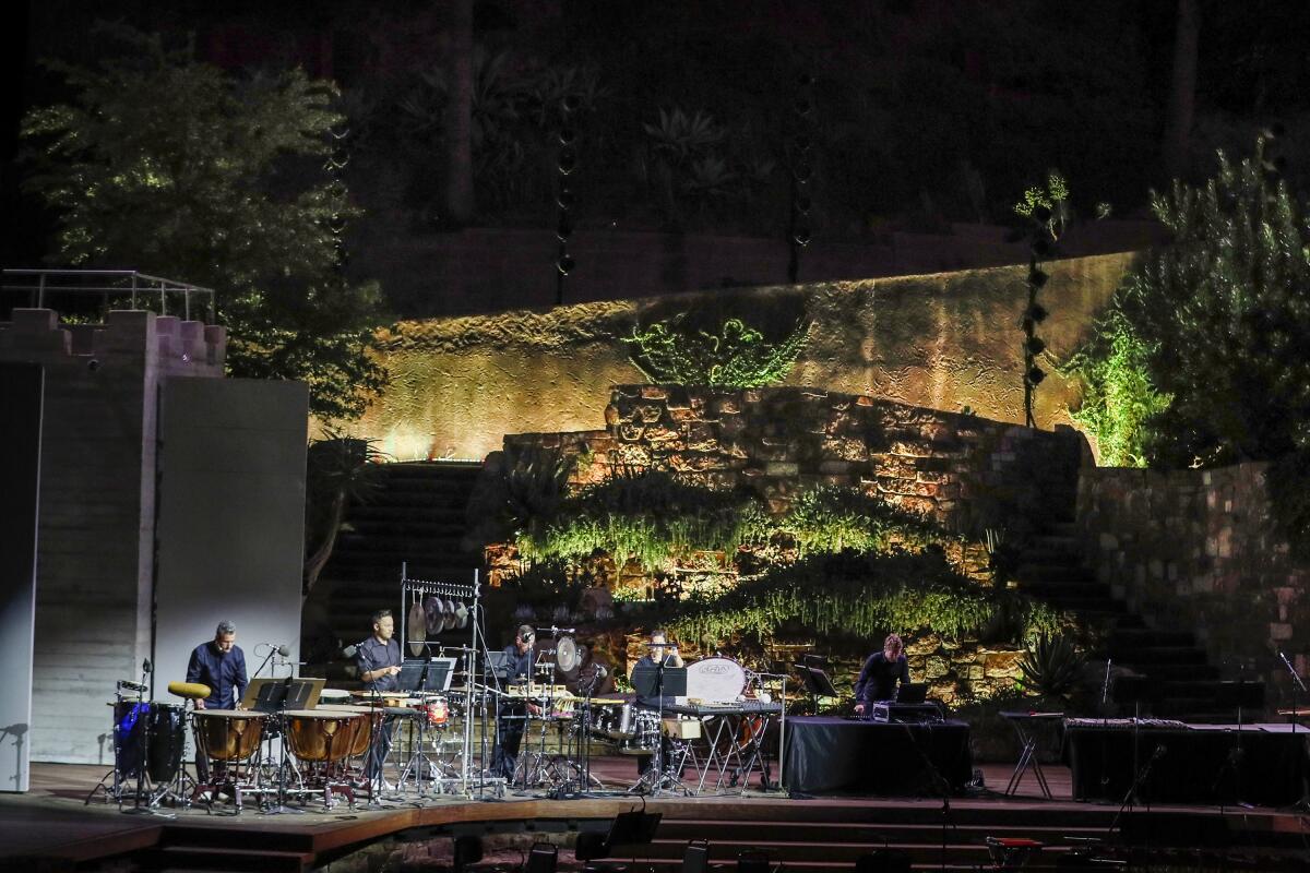 A group of percussionists perform on an outdoor stage.