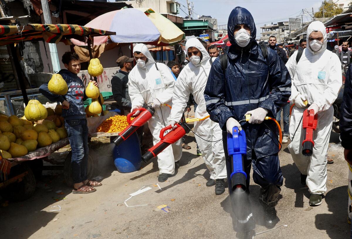 Workers wearing protective gear spray disinfectant at the main market in Gaza City on Thursday.