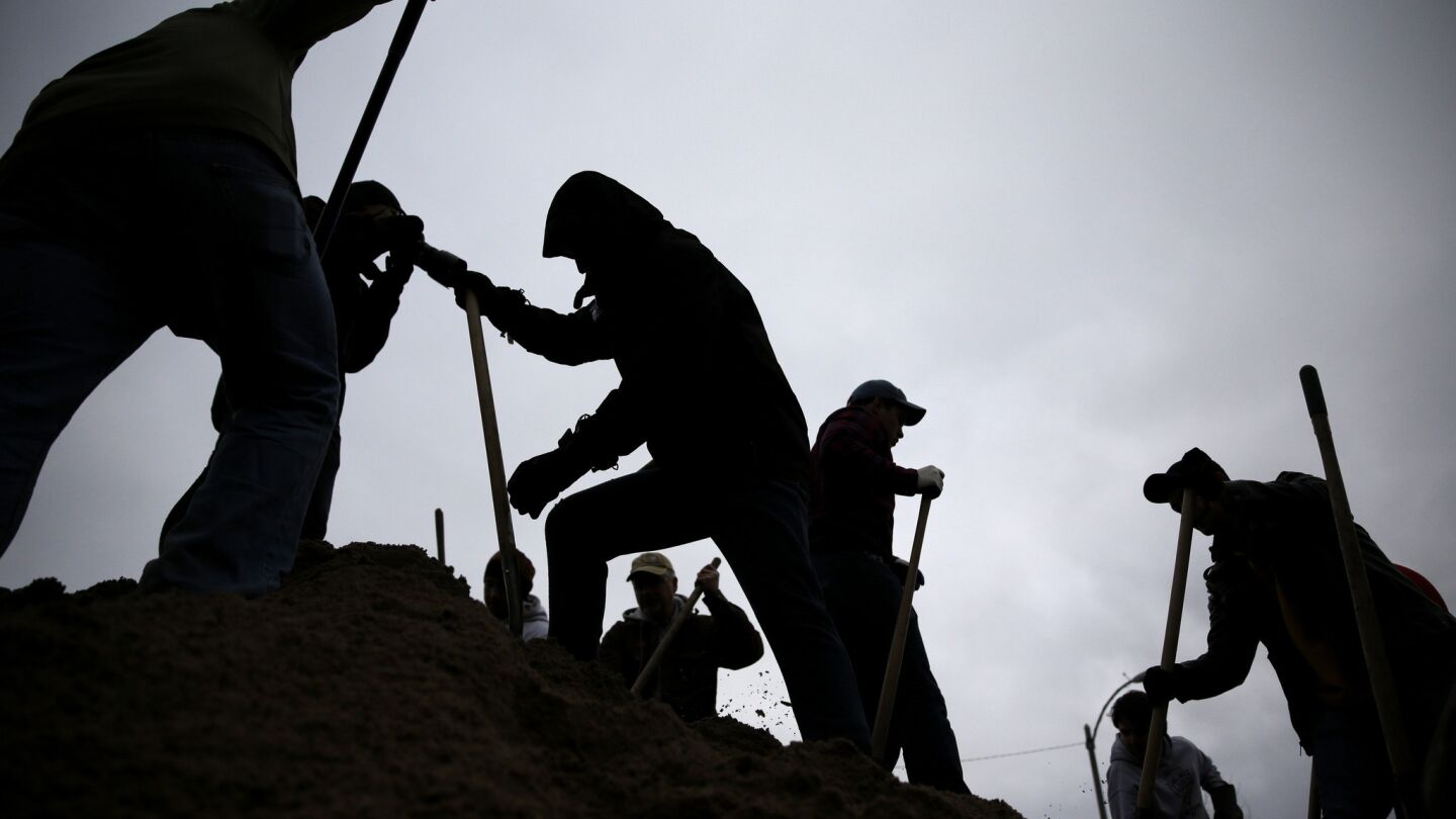 Against a gray winter sky, volunteers use shovels atop a pile of sand as they help fill sandbags in St. Louis.