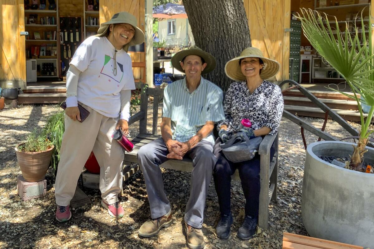 Three people in sun hats volunteering pose in front of a tree at Theodore Payne Foundation. 