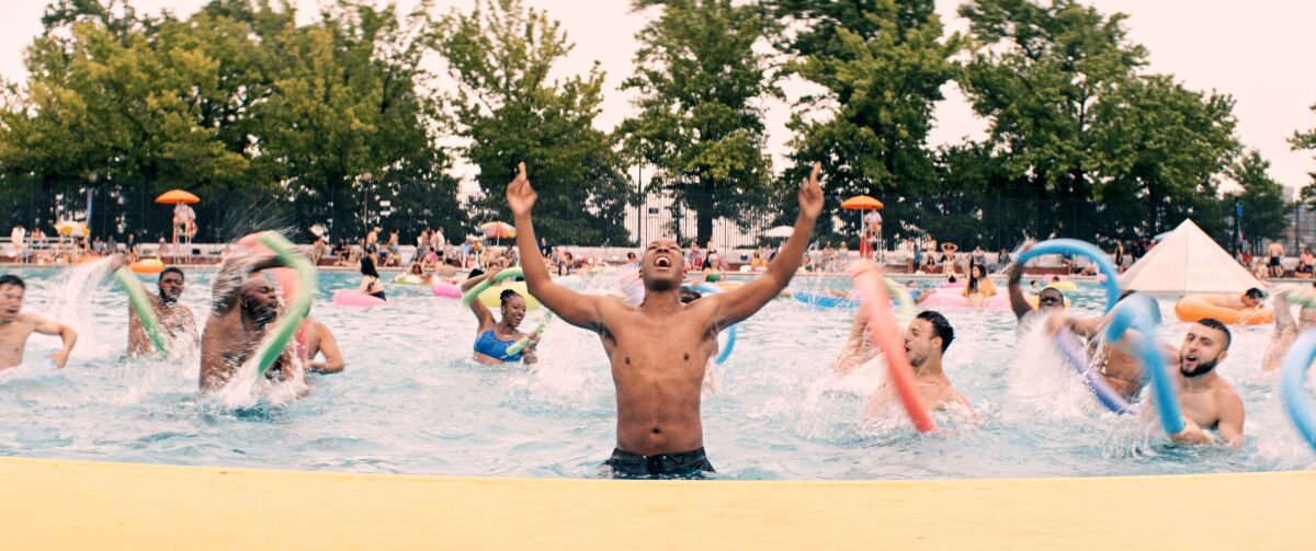 Corey Hawkins splashes in a pool with a group of dancers in a scene from "In the Heights"