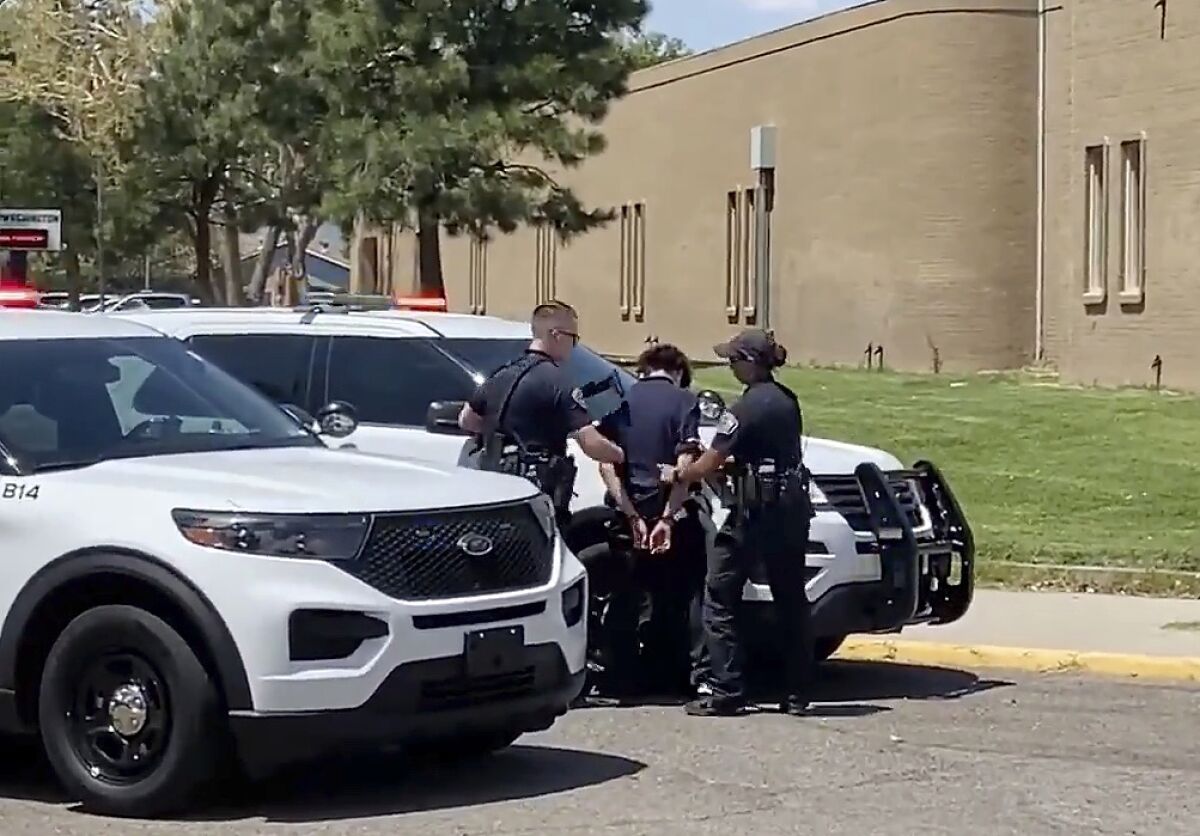 In this image from taken from video courtesy of Ryan Laughlin/KOB 4 TV Albuquerque Police Department officers search a student after a shooting at Washington Middle School which left at least one student dead and another in custody, police said Friday, Aug. 13, 2021. Only a few days into the new school year and New Mexico's largest district was left reeling from the shooting. Authorities said Friday's shooting was an isolated incident between two Washington Middle School students who were believed to be about 13 years old. (Ryan Laughlin/KOB 4 TV via AP)