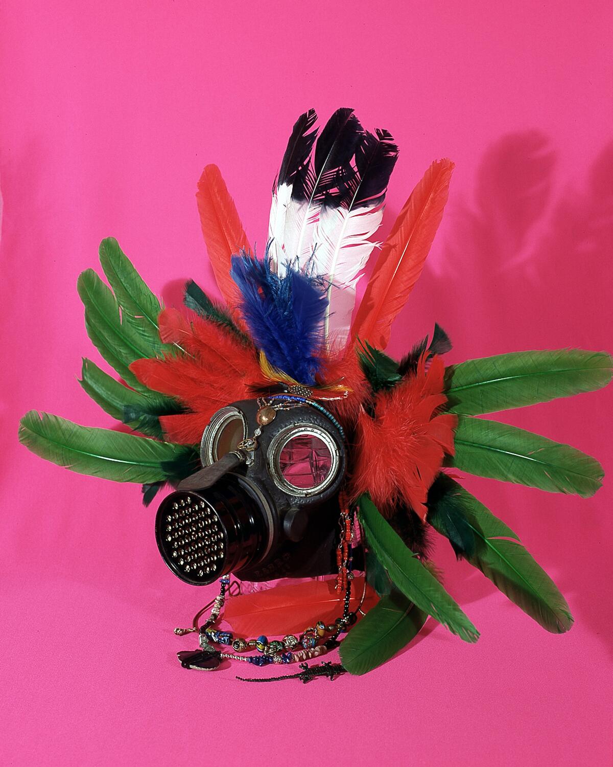 An old gas mask is studded with large, soft feathers, with strings of beads that dangle from the area around the temples