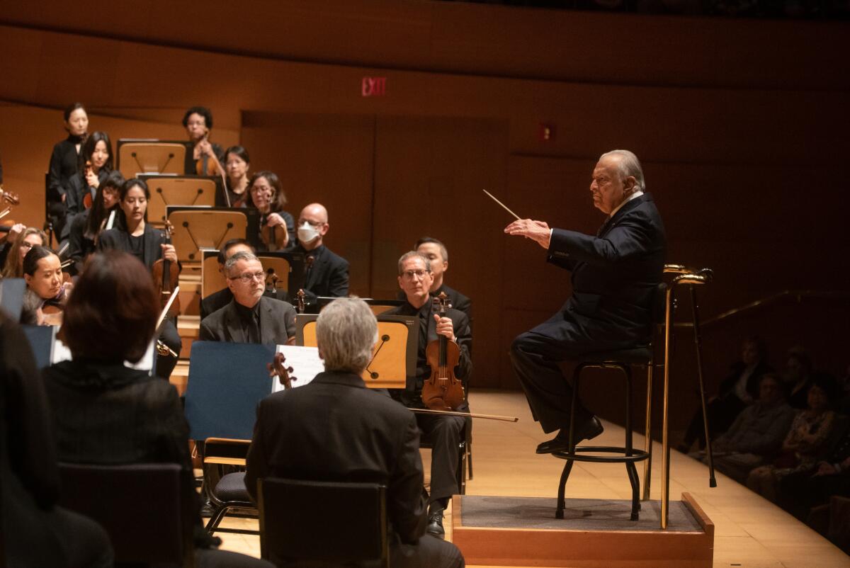 Zubin Mehta, wearing black and sitting on a stool, conducts the L.A. Phil