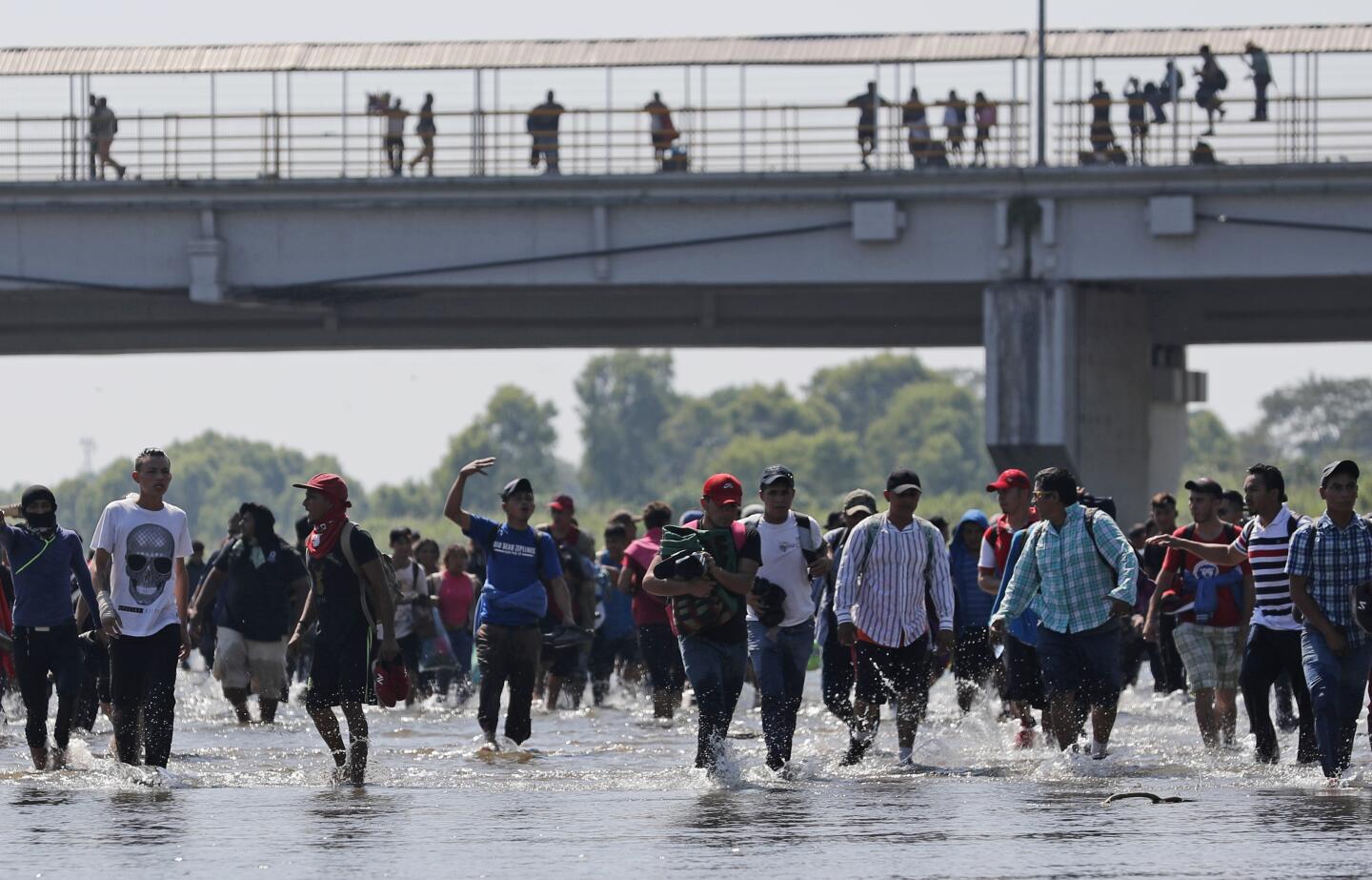 Central American migrants wade across the Suchiate River from Guatemala to Mexico as others stand on the legal border crossing bridge, near Ciudad Hidalgo, Mexico.