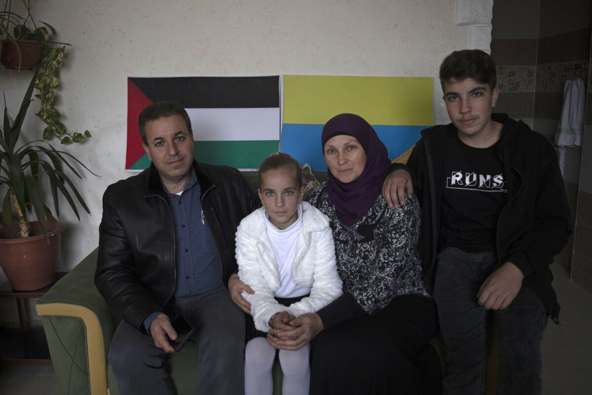 Ukrainian Oksana al-Astal sits with her Palestinian husband and their children as they pose for a photo in front of representations of Palestinian and Ukrainian flags decorating the living room of their home in Khan Younis, southern Gaza Strip, Sunday, March 13, 2022. The al-Astal family is among dozens of Palestinian-Ukrainian families in the isolated territory who have experienced several wars firsthand — the most recent last May — and are now watching another unfold in Ukraine, where many of them have loved ones. (AP Photo/ Khalil Hamra)