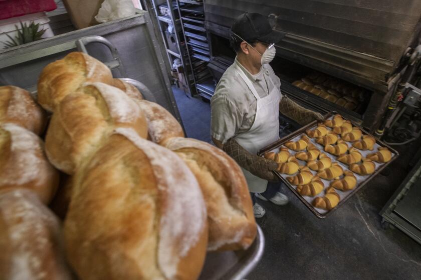 EAST LOS ANGELES, CA - APRIL 07, 2021: Miguel Dominguez, owner of Marisol Bakery on Whittier Blvd. in East Los Angeles, carries a tray of fresh baked pastries out of the oven. Dominguez says that the bakery has been struggling even worse than last year and he expected things to get better once people started to get vaccinated but that hasn't been the case. (Mel Melcon / Los Angeles Times)