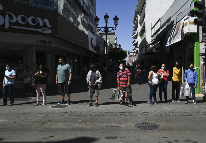 Wearing masks to curb the spread of the new coronavirus, people wait for a traffic light to change before crossing a street in San Jose, Costa Rica, Tuesday, Jan. 18, 2022. (AP Photo/Carlos Gonzalez)
