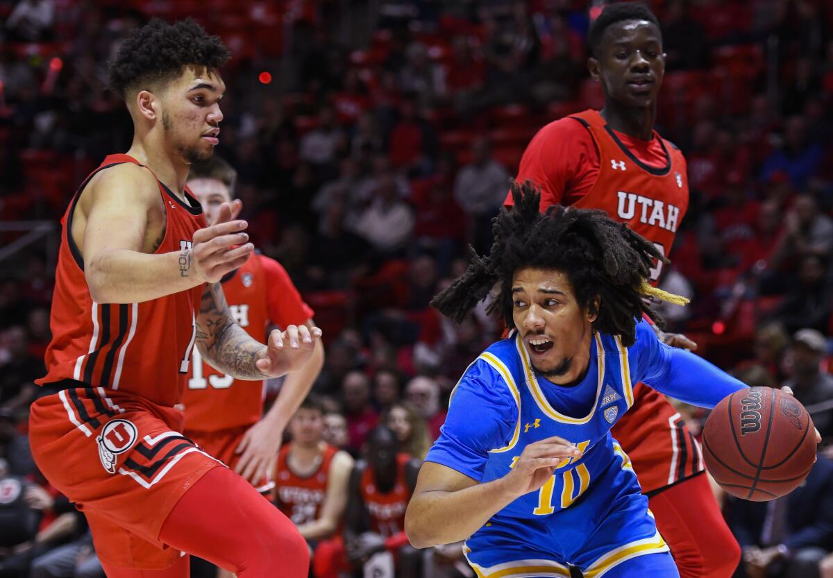 UCLA guard Tyger Campbell drives between Utah's Timmy Allen, left, and Lahat Thioune during a game Feb. 20 in Salt Lake City. 
