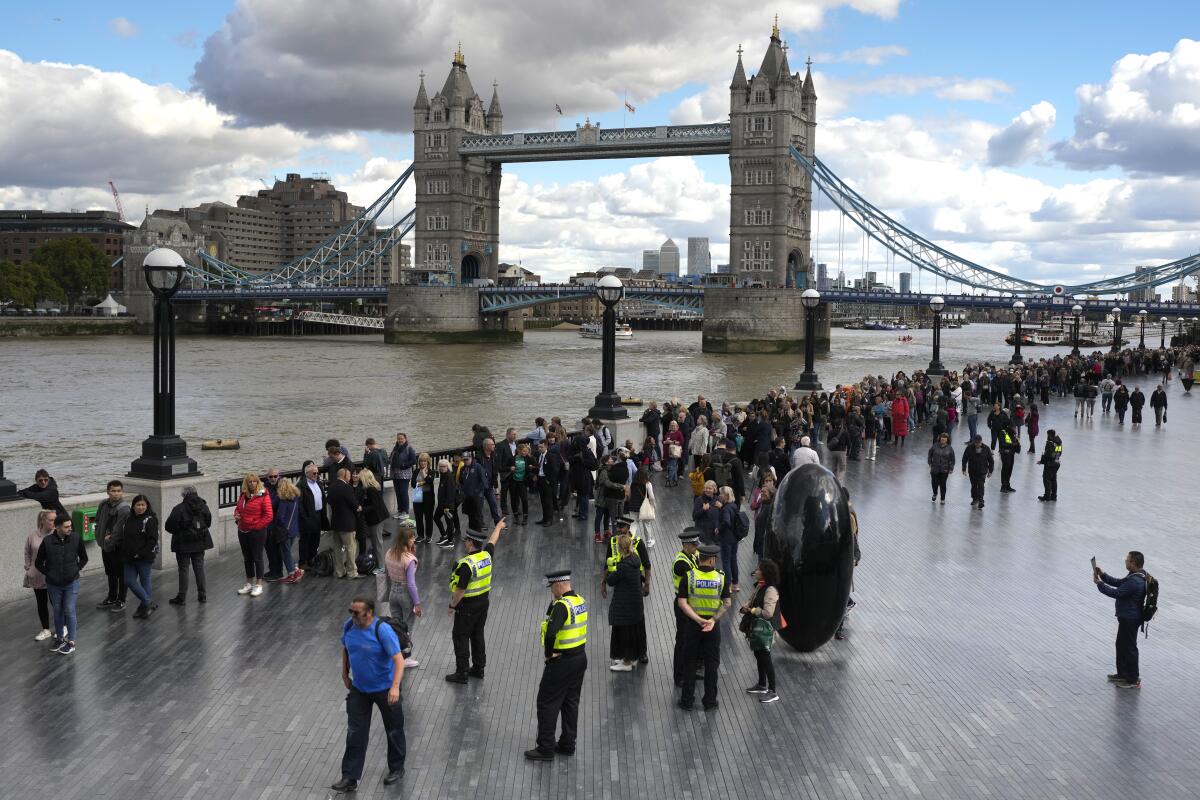 A line of people standing before a river with Tower Bridge in the background.