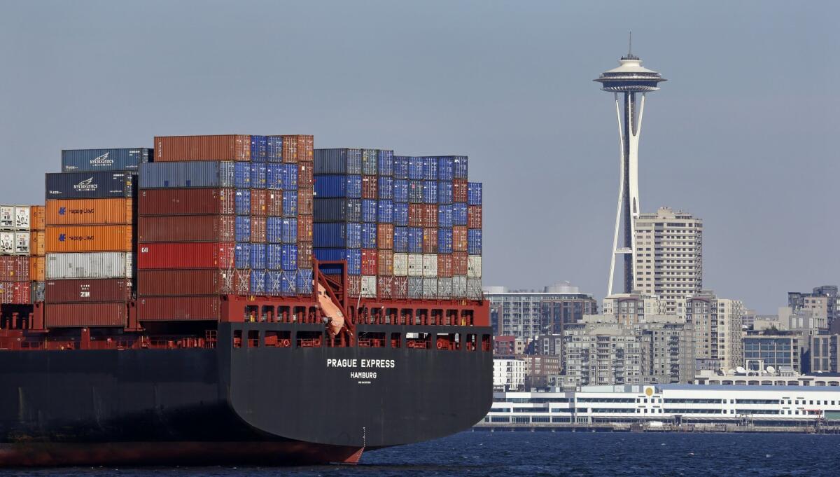The Space Needle towers in the background beyond a container ship anchored in Elliott Bay near downtown Seattle.