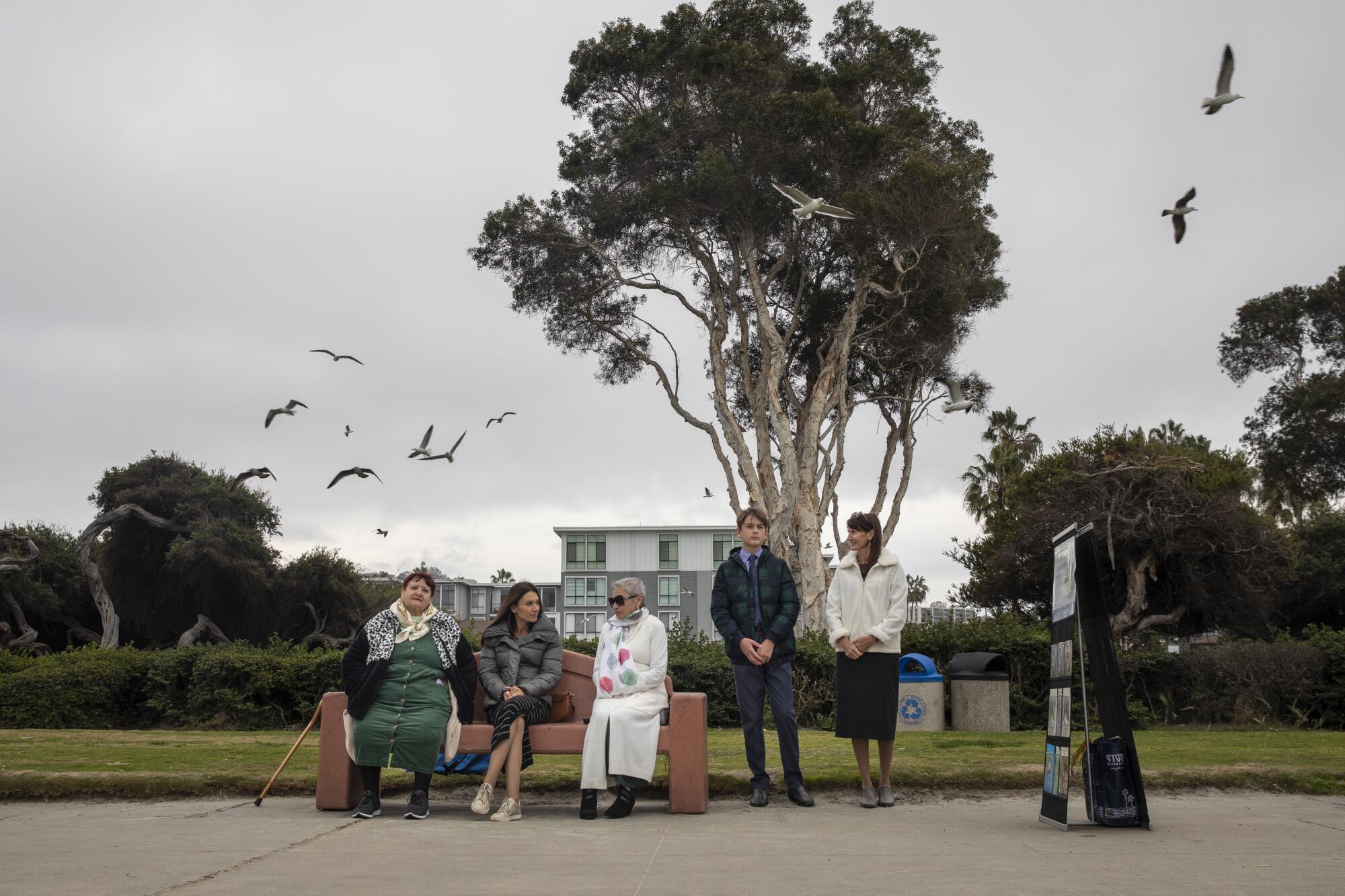 Three people sit on a bench and two stand next to a display of Jehovah's Witnesses pamphlets in La Jolla Shores