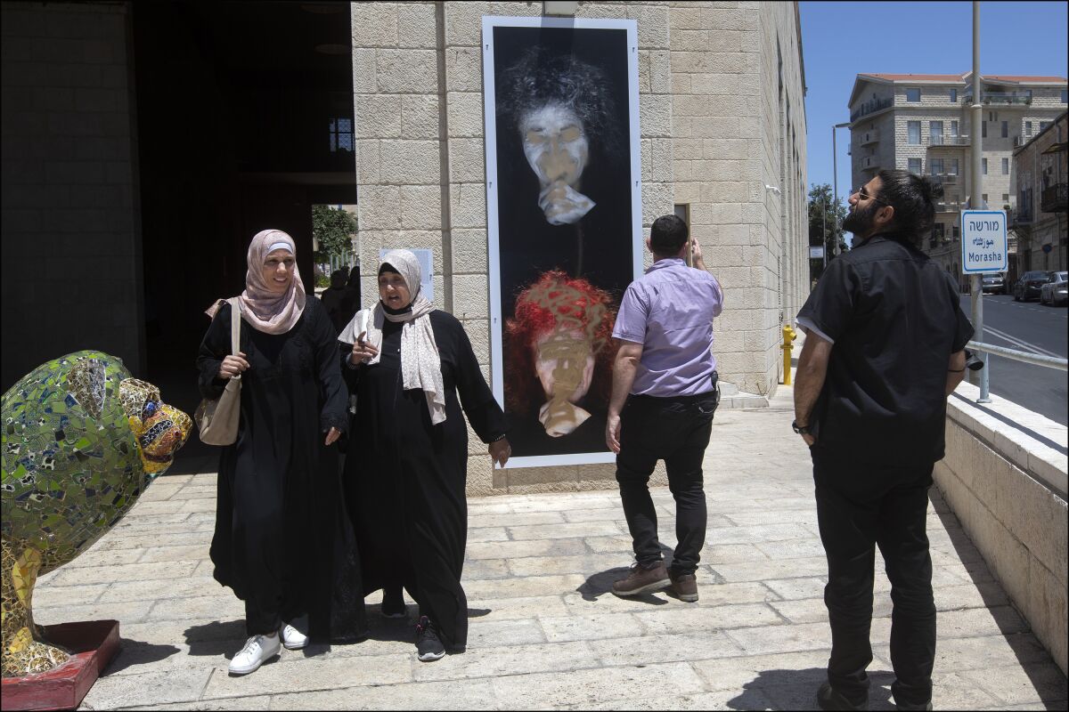In this July 1, 2021, photo provided by the The Lonka Project, people look at the defaced portrait of Holocaust survivor Peggy Parnass, outside Jerusalem City Hall, where it is on display as part of an exhibit that tells the stories of 400 survivors of the Nazi atrocities during World War II in The Lonka Project exhibition in Safra Square in Jerusalem. Israel is having a difficult time keeping images of women in public from being defaced. Billboards showing women -- whether they are soccer players, musicians or young girls -- have been repeatedly defaced and torn down by religious extremists in Jerusalem and other cities. (Jim Hollander/The Lonka Project via AP)