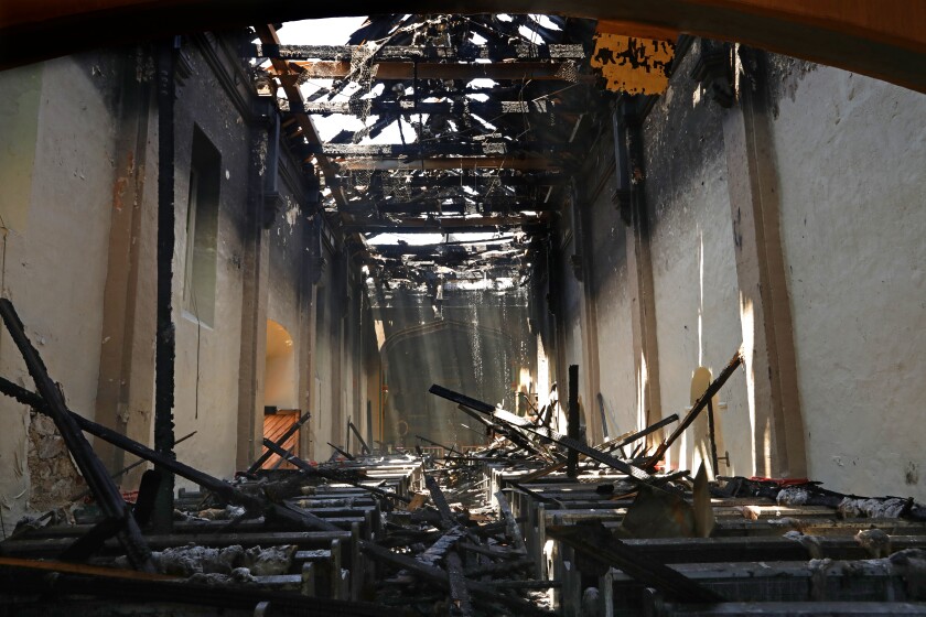 Sunlight beams through the destroyed roof onto charred pews inside the San Gabriel Mission Church