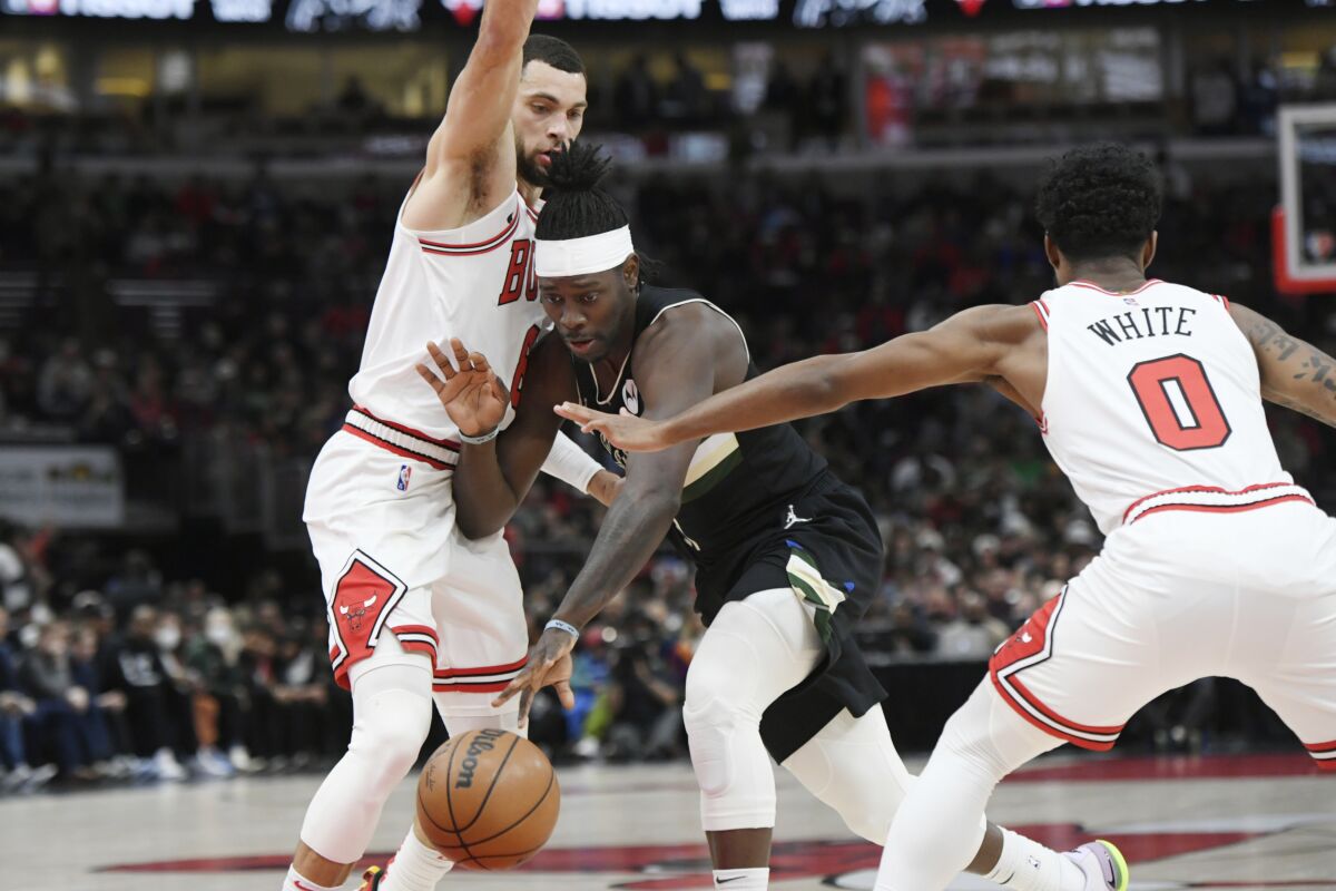 Milwaukee Bucks guard Jrue Holiday (21) drives against Chicago Bulls' Zach LaVine (8) and Coby White (0) during the first half of an NBA basketball game Friday, March 4, 2022, in Chicago. (AP Photo/Paul Beaty)