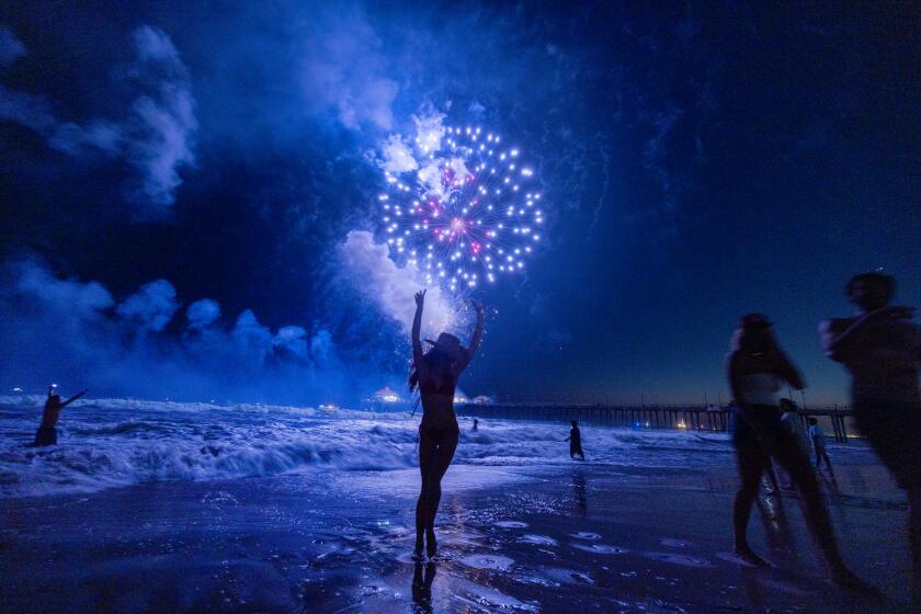 Huntington Beach, CA - July 04: Carli Dugan, of San Louis Obispo, dances in the water while watching the sky light up with fireworks over the ocean and pier on Independence Day, 4th of July in Huntington Beach Thursday, July 4, 2024. (Allen J. Schaben / Los Angeles Times)