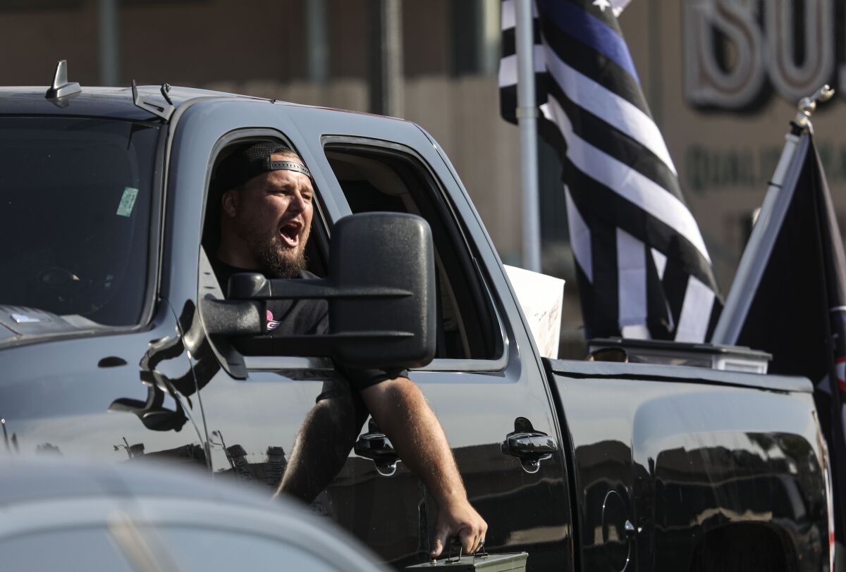 A man leans out of his pickup truck, with a Blue Lives Matter flag in the bed, yelling at protesters