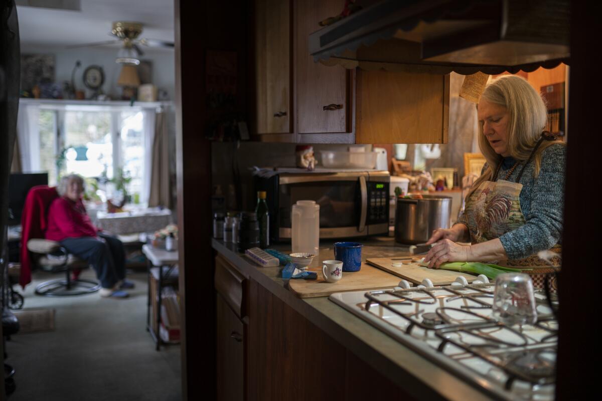 Nancy Rose, right, who contracted COVID-19 in 2021 and continues to exhibit long-haul symptoms including brain fog and memory difficulties, cooks for her mother, Amy Russell, left, at their home, Tuesday, Jan. 25, 2022, in Port Jefferson, N.Y. Rose, 67, said many of her symptoms waned after she got vaccinated, though she still has bouts of fatigue and memory loss. (AP Photo/John Minchillo)