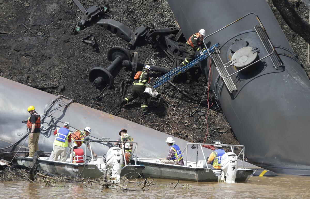 Workers remove damaged tanker cars along the tracks where a train carrying crude oil derailed Wednesday and caught fire along the James River near downtown Lynchburg, Va.