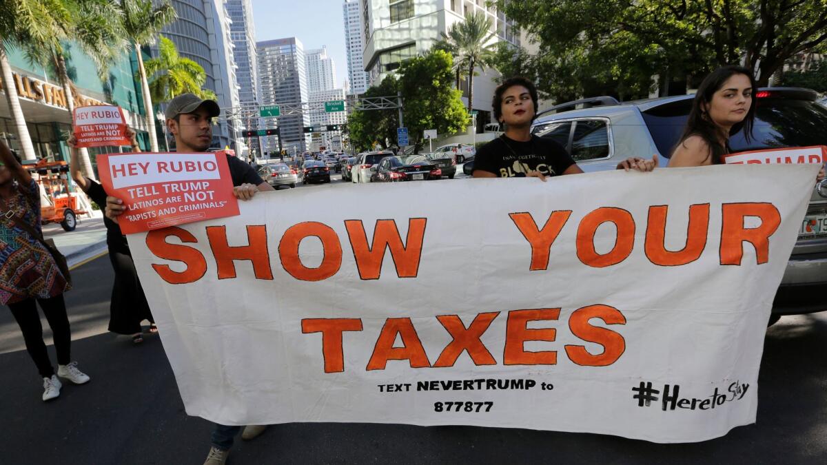 Marching protesters hold up a sign demanding that Republican presidential candidate Donald Trump release his tax returns, in Miami on Sept. 16.