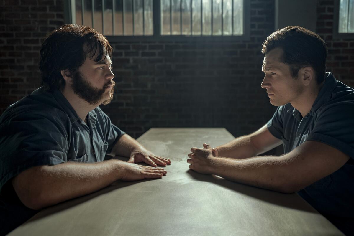 Paul Walter Hauser and Taron Egerton sit across a table wearing jail jumpsuits in "Black Bird."