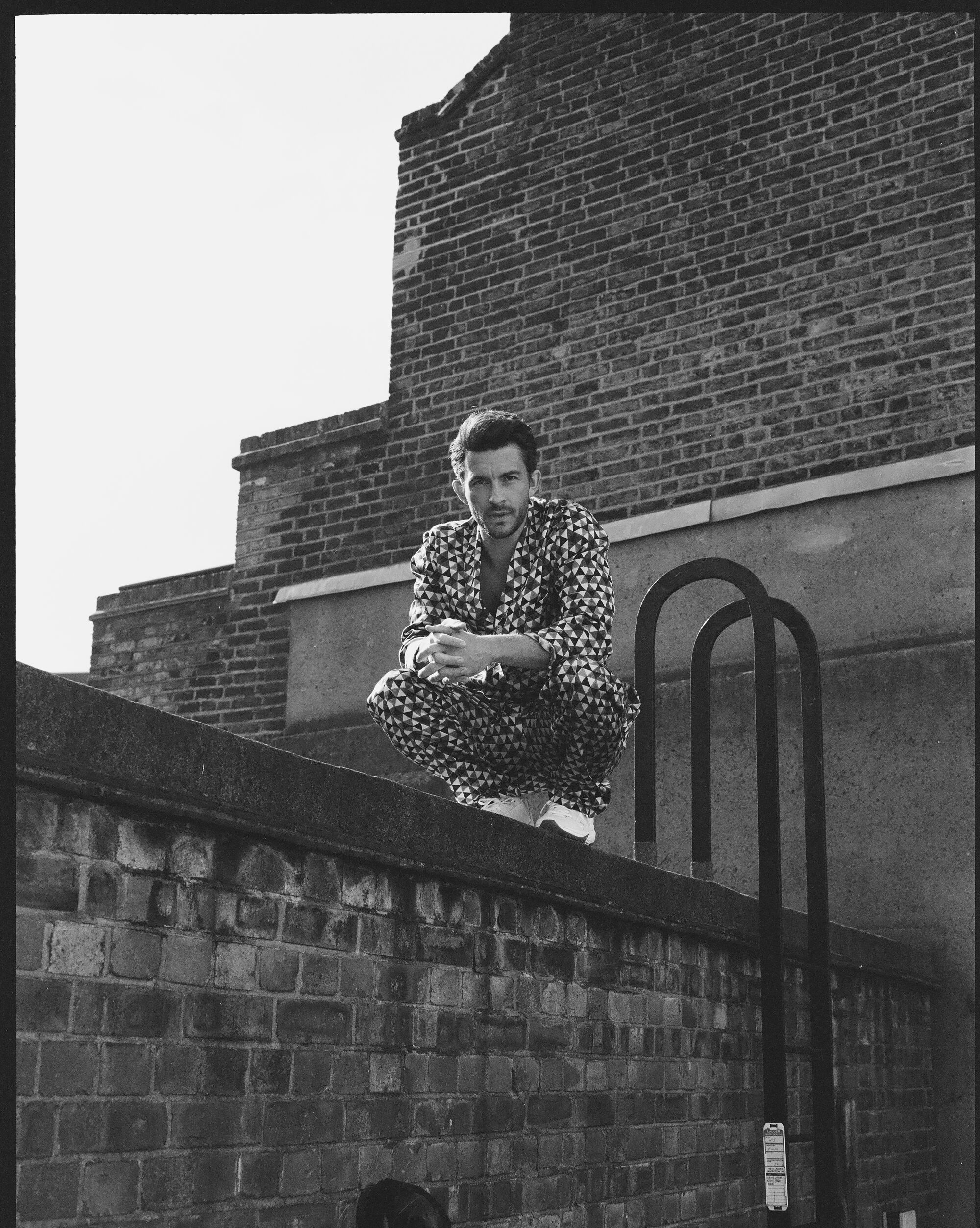 A man crouches on a rooftop wearing patterned, silk clothing.