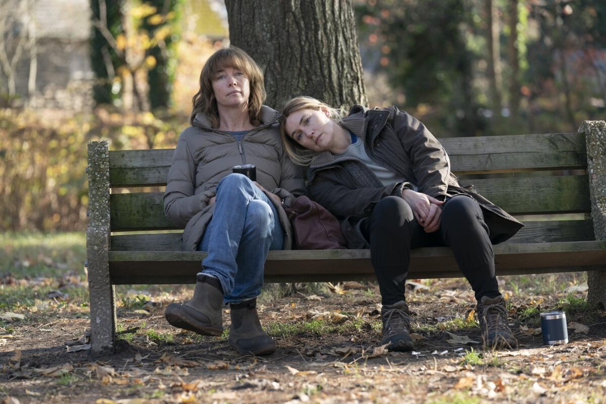 A woman leans on another woman's shoulder on a park bench