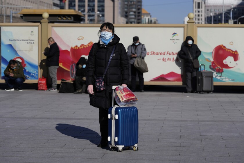 A traveler waits outside the Beijing railway station with her suitcase in Beijing, China, Friday, Jan. 28, 2022. The Beijing Winter Olympics is coinciding with the Chinese Lunar New Year and renewed Covid outbreaks prompting the Chinese authorities to call on the public to stay where they are instead of traveling to their hometowns for the year's most important family holiday. (AP Photo/Ng Han Guan)